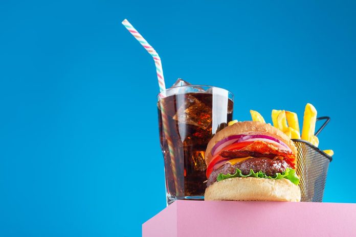 Fresh juicy beef hamburger, fried potatoes and drink, placed on the stand and blue background. Copy space for text, trendy hero view