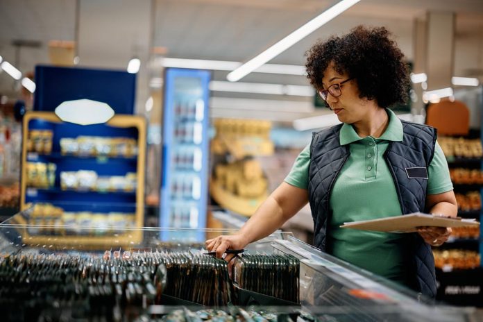 Female store manager inspecting food while working in refrigerated compartment at supermarket.