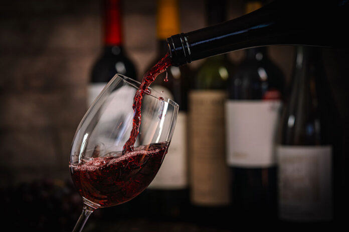pouring-red-wine-into-glass-with-bottles-and-grape-2026