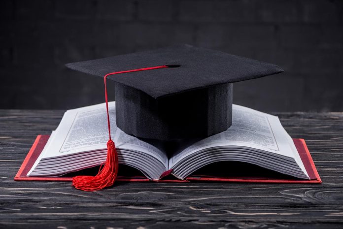 Open book with graduation cap on wooden table
