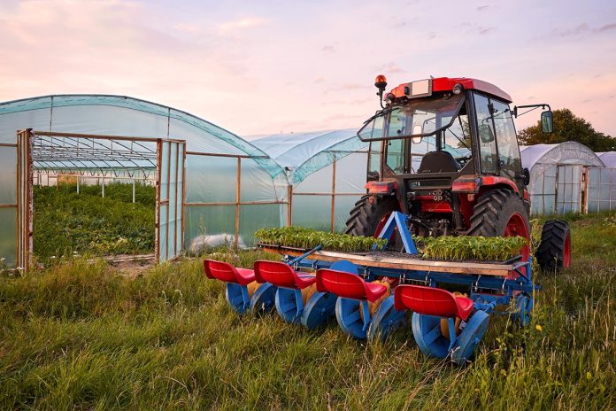 Manual seedling planter mounted to a tractor in front of greenho